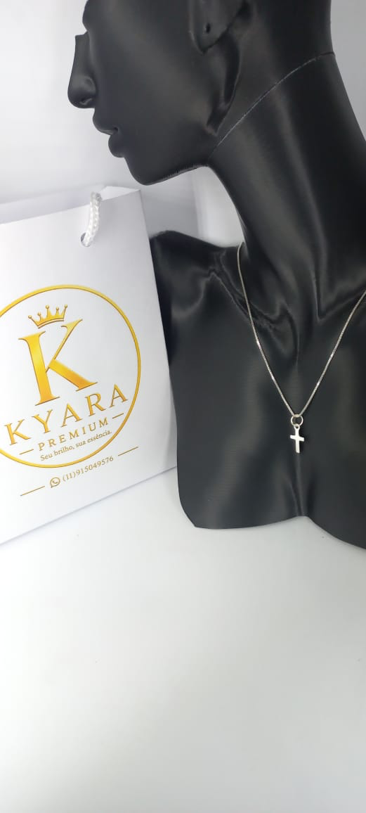 Colar Cruz da Fé em Prata 925 ao lado da sacola Kyara Premium